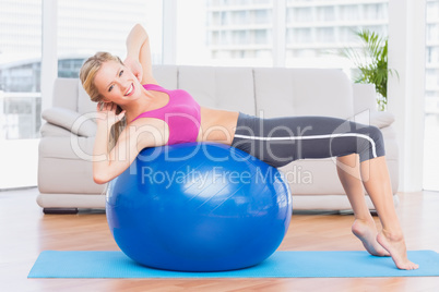 Slim blonde doing sit ups on exercise ball smiling at camera