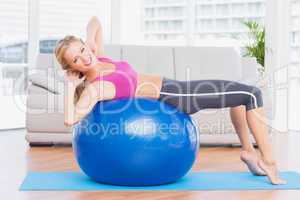 Slim blonde doing sit ups on exercise ball smiling at camera