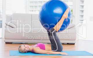 Slim blonde holding exercise ball between legs