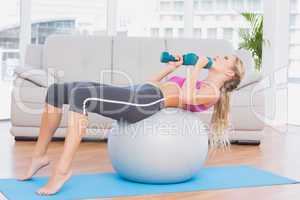 Smiling blonde doing sit ups with exercise ball holding dumbbell