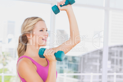 Fit blonde lifting dumbbells and smiling