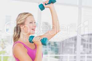 Fit blonde lifting dumbbells and smiling