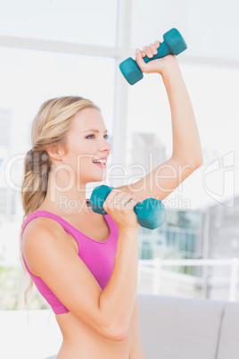 Toned blonde lifting dumbbells and smiling