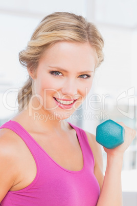 Cute blonde lifting dumbbells and smiling at camera