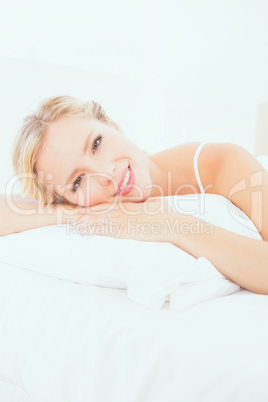 Cheerful young blonde lying on her bed smiling at camera