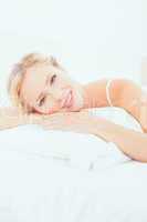 Cheerful young blonde lying on her bed smiling at camera