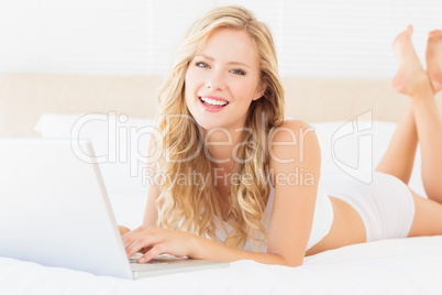 Happy young blonde lying on her bed using laptop Happy young blonde lying on her bed using laptop