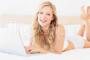 Happy young blonde lying on her bed using laptop