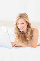 Cheerful young blonde lying on her bed using laptop