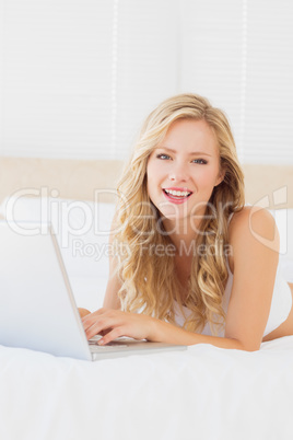 Smiling young blonde lying on her bed using laptop