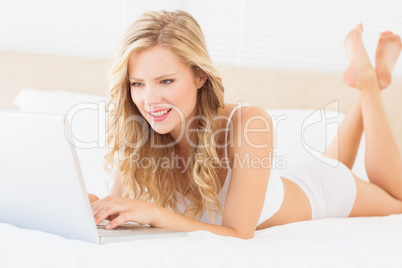 Pretty young blonde lying on her bed using laptop