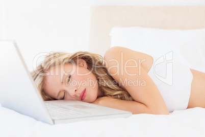 Pretty young blonde sleeping beside her laptop