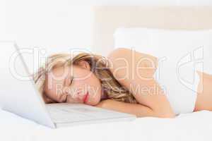 Pretty young blonde sleeping beside her laptop