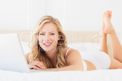 Smiling young blonde using her laptop on bed Smiling young blonde using her laptop on bed