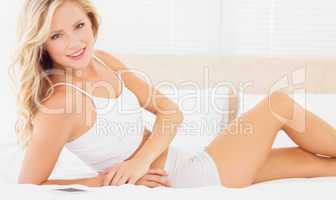 Fit blonde woman lying on bed smiling at camera