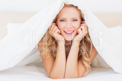 Attractive blonde smiling at camera from under the duvet