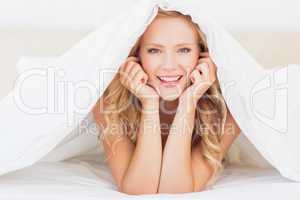 Attractive blonde smiling at camera from under the duvet