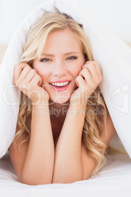 Pretty blonde smiling at camera from under the duvet