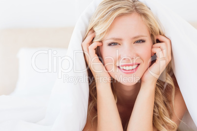 Cute blonde smiling at camera from under the duvet