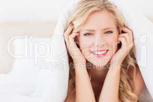 Cute blonde smiling at camera from under the duvet