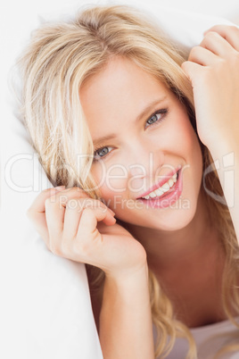 Pretty young blonde smiling at camera from under the sheet