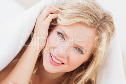 Pretty young blonde smiling at camera from under the duvet