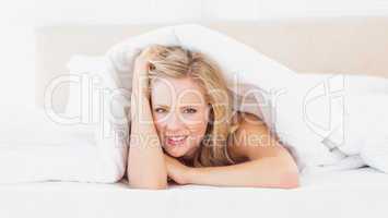 Cute young blonde smiling at camera from under the sheet