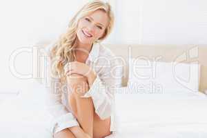 Beautiful young blonde in white shirt smiling at camera sitting