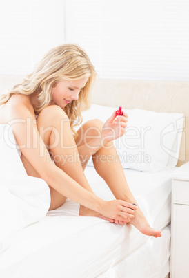 Pretty young blonde painting her toenails at edge of bed