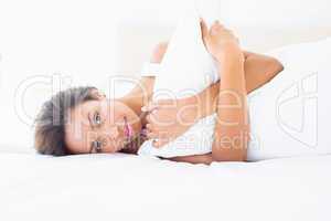 Smiling brunette lying on bed hugging pillow