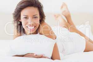 Smiling pretty brunette lying on bed holding pillow