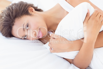 Smiling pretty brunette lying on bed hugging pillow