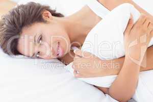 Smiling pretty brunette lying on bed hugging pillow