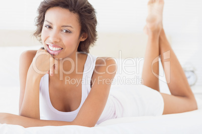 Happy brunette lying on bed smiling at camera