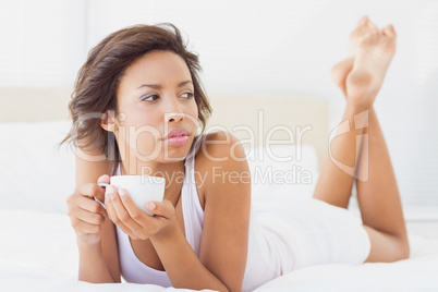 Pretty brunette lying on bed thinking holding a cup