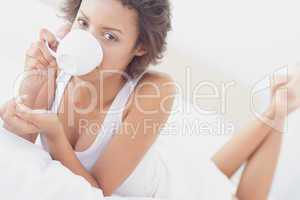 Pretty brunette lying on bed drinking cup of coffee
