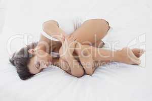 Unhappy brunette lying on her bed hugging her knees