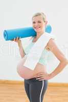 Pregnant blonde smiling at camera holding exercise mat