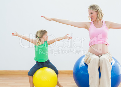 Pregnant woman bouncing on exercise ball with young daughter