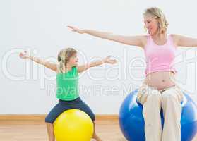 Pregnant woman bouncing on exercise ball with young daughter