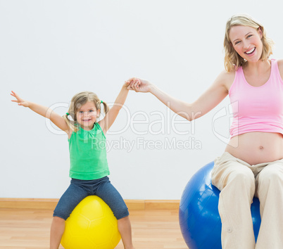 Happy pregnant woman bouncing on exercise ball with young daught