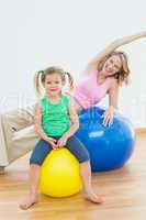 Happy pregnant woman exercising on exercise ball with young daug