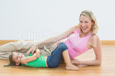 Smiling pregnant woman tickling young daughter looking at camera