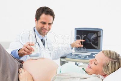 Happy doctor showing blonde pregnant woman her baby on sonagram
