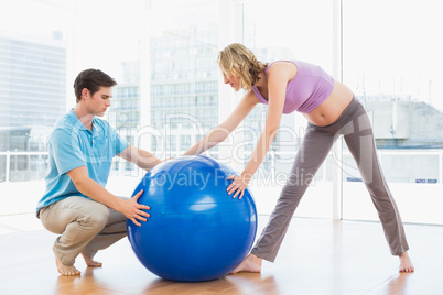 Blonde pregnant woman exercising with trainer and ball