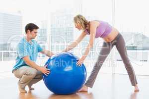 Blonde pregnant woman exercising with trainer and ball