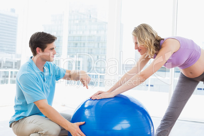 Happy pregnant woman exercising with trainer and ball