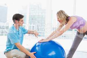 Happy pregnant woman exercising with trainer and ball