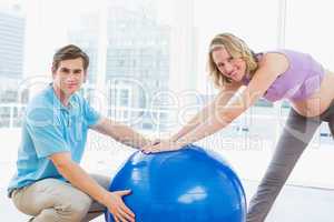 Smiling pregnant woman exercising with trainer and ball