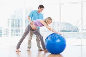 Trainer exercising with blonde pregnant client and exercise ball